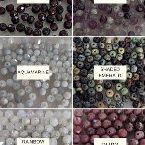 May include: A collection of faceted gemstone beads organized in six labeled sections: dark red Garnet, light purple Amethyst, pale blue Aquamarine, multi-colored Shaded Emerald, translucent white Rainbow Moonstone, and deep pink Ruby beads.