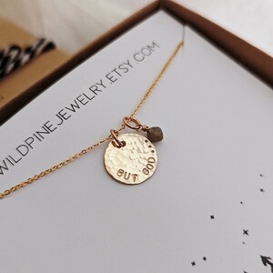 May include: Gold necklace with a hammered disc pendant that says "But God" and a small green gemstone charm. The necklace is in a white box with the text "Wildpine Jewelry Etsy.com" printed on it.