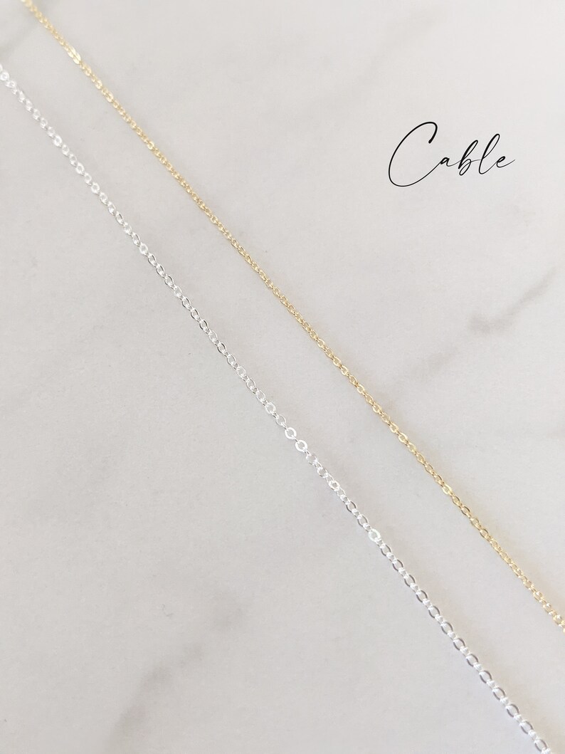 May include: Two cable chains, one silver and one gold, are shown against a white background. The word "Cable" is written in black script at the top of the image.