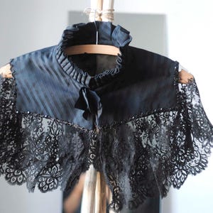 May include: A black lace collar with a striped satin lining. The collar has a high neckline and a scalloped edge.