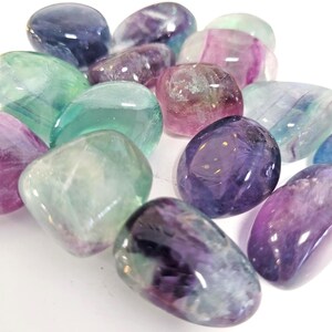 May include: A selection of polished fluorite stones in shades of green, purple, and pink. The stones are smooth and rounded, with a translucent appearance. The image is a close-up, showcasing the natural beauty of the gemstones. The stones are measured in centimetres.