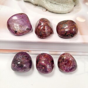 Puede incluir: Seis piedras preciosas pulidas y rodadas en tonos rojo intenso y p&uacute;rpura. Las piedras tienen una forma suave y redondeada y un acabado brillante. Las piedras est&aacute;n dispuestas sobre una superficie blanca, con un fondo neutro.