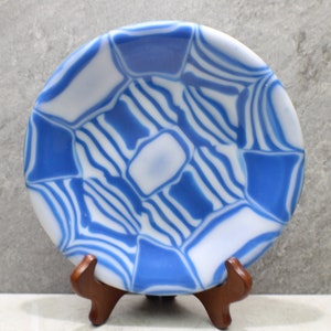 May include: A blue and white glass plate with a swirling pattern. The plate is on a wooden stand.