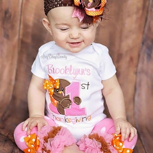 May include: A baby wearing a white onesie with a turkey graphic and the text "Brooklynn's 1st Thanksgiving." The outfit includes pink polka dot pants with ruffles and a matching headband with a turkey and bow.
