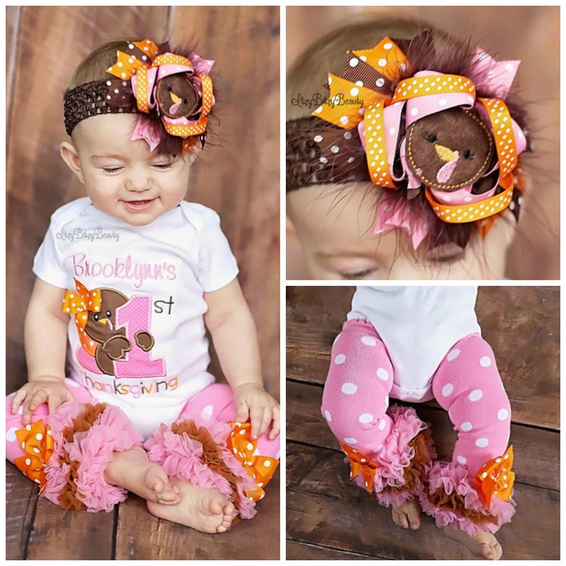 May include: A baby wearing a white bodysuit with the text "Brooklyn's 1st Thanksgiving", paired with pink polka dot pants and a matching headband. The headband and pants feature turkey and bow accents in brown, orange, and pink.
