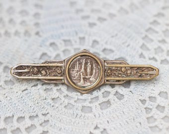 Puede incluir: Un broche de tono plateado y dorado con un diseño floral detallado y un medallón central que presenta una imagen religiosa de la Virgen María.