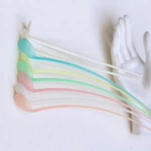 Może przedstawiać: Rzeźba ścienna przedstawiająca białą dłoń trzymającą sześć pastelowych obiektów w kształcie nut. Nuty są w odcieniach niebieskiego, zielonego, żółtego, różowego i pomarańczowego, tworząc kapryśną i artystyczną ekspozycję.