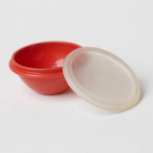 以下が含まれることがあります： 赤いプラスチック製のボウルと透明なプラスチック製の蓋。ボウルは丸く、表面は滑らかです。蓋も丸く、表面は滑らかです。