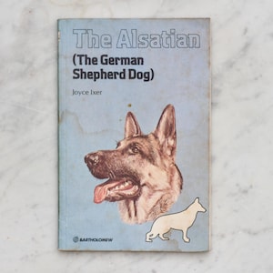 May include: A book cover with a blue background and the title "The Alsatian (The German Shepherd Dog)" by Joyce Ixer. The cover features a drawing of a German Shepherd dog.