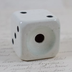 May include: White ceramic dice with black dots. The dice has a hole in the center.