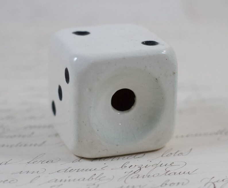 May include: White ceramic dice with black dots. The dice has a hole in the center.