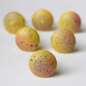 May include: Six yellow speckled round ornaments with a colorful splatter paint design.