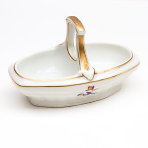 Peut inclure: Un panier en porcelaine blanche avec une poignée dorée et un motif floral. Le panier est de forme ovale et possède une petite lèvre autour du haut.