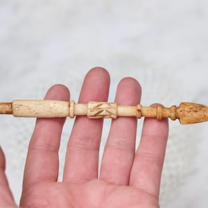 Op de afbeelding: Een gesneden beenwerktuig met een puntige punt en ingewikkelde details. Het gereedschap is gemaakt van lichtbruin been en heeft een gladde, gepolijste afwerking.