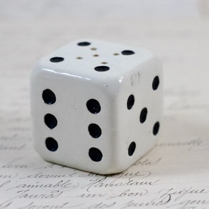 May include: White ceramic dice with black dots. The dice has six sides and is a decorative object.