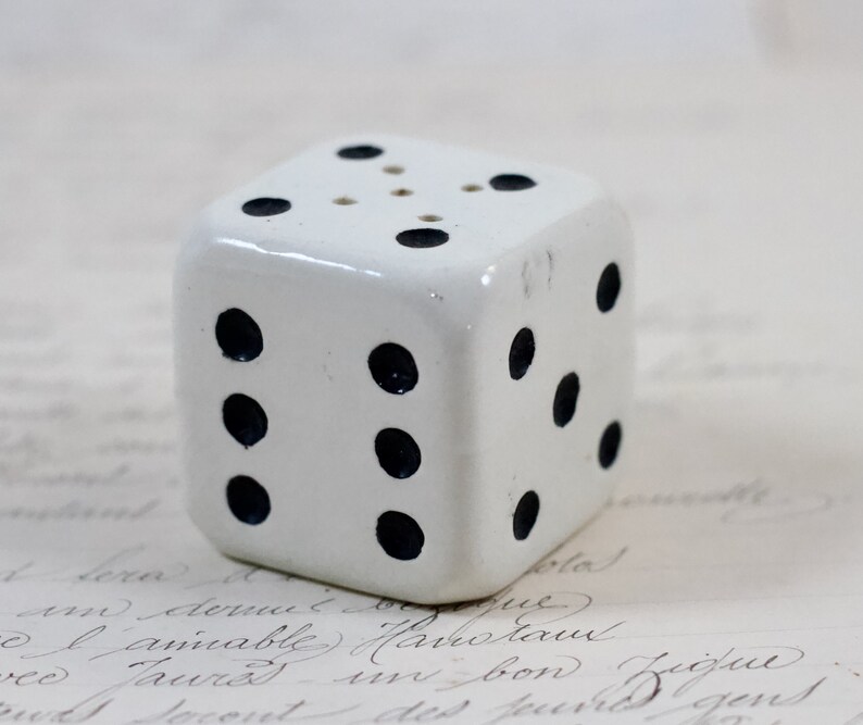 May include: White ceramic dice with black dots. The dice has six sides and is a decorative object.