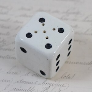 May include: White ceramic dice with black dots. The dice has six sides and is about 2 inches tall.