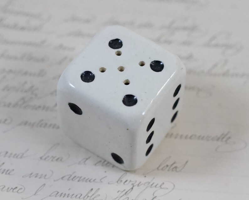 May include: White ceramic dice with black dots. The dice has six sides and is about 2 inches tall.