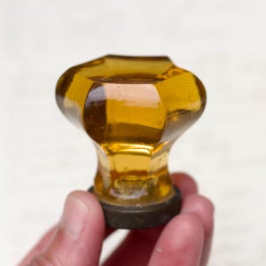 May include: A vintage amber glass cabinet knob with a faceted design and a black metal base.