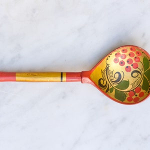 May include: A traditional wooden spoon with a red and gold handle and a painted design of red berries and green leaves on the bowl.