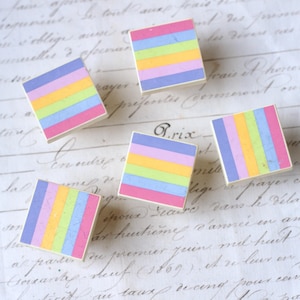 May include: A collection of colorful sticky notes arranged on a vintage paper background. Each square note features horizontal stripes in shades of pink, yellow, green, blue, and purple. The notes are approximately 1.5 inches square.