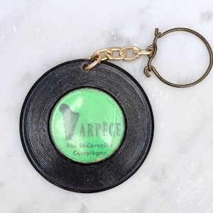 May include: Black and green vinyl record keychain with the text "ARPECE Rue St-Cermeille Compiègne".