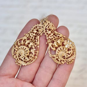 Könnte beinhalten: Ein Paar goldene Filigranohrringe mit filigranen Blumendesigns. Die Ohrringe sind zart und kunstvoll, mit einer Vintage-Ästhetik.