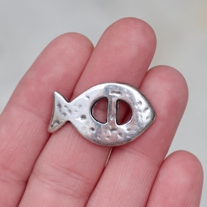 Può includere: Ciondolo a forma di pesce d'argento con una superficie testurizzata e un foro al centro. Il ciondolo è lungo circa 2,5 cm.