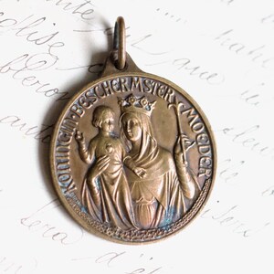 Puede incluir: Un colgante de bronce con un relieve de la Virgen Mar&iacute;a y el ni&ntilde;o Jes&uacute;s. El colgante est&aacute; inscrito con las palabras "Mutter Gottes" y "Jungfrau-Bescher-Mutter".