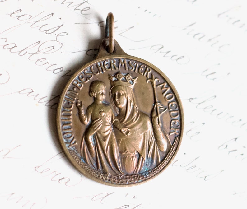 Puede incluir: Un colgante de bronce con un relieve de la Virgen Mar&iacute;a y el ni&ntilde;o Jes&uacute;s. El colgante est&aacute; inscrito con las palabras "Mutter Gottes" y "Jungfrau-Bescher-Mutter".
