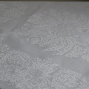 Peut inclure: Nappe en damassé blanc avec un motif floral. La nappe présente un design délicat et complexe avec un motif répétitif de fleurs et de feuilles.