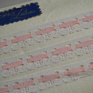 May include: Three rows of white lace trim with pink stripes. The trim is on a white background with a blue label that says "Wentex Laces".