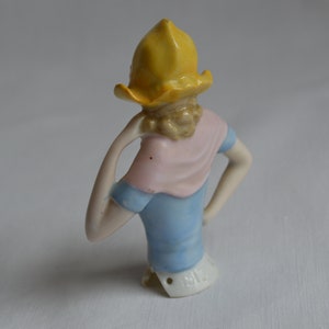 Pode incluir: Uma boneca de porcelana com um chap&eacute;u amarelo, um len&ccedil;o rosa e um vestido azul. A boneca est&aacute; faltando a parte inferior do corpo e tem uma marca na parte inferior que diz "1514".