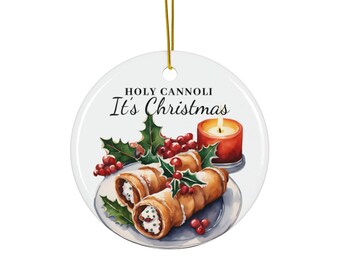 May include: A white, round Christmas ornament with a gold string. The ornament features a watercolor illustration of cannoli, holly, berries, and a lit candle. Text on the ornament reads "HOLY CANNOLI It's Christmas."