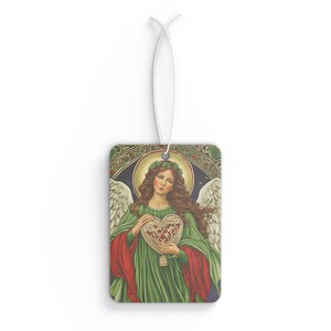 May include: A Christmas-themed car air freshener featuring an angel with a halo of holly leaves holding a heart-shaped ornament. The angel is wearing a green gown with a red cape and has long brown hair.