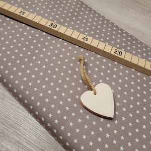 Könnte beinhalten: Ein brauner Stoff mit einem weißen Sternenmuster. Ein weißes herzförmiges Ornament hängt an dem Stoff.