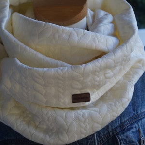 Könnte beinhalten: Ein weißer Infinity-Schal mit einem strukturierten Blumenmuster. Der Schal ist aus einem weichen, komfortablen Stoff gefertigt und hat ein braunes Leder-Etikett mit dem Text "Handmade with Love".