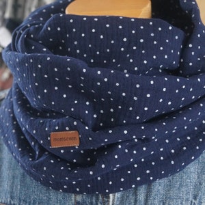 Könnte beinhalten: Ein marineblauer Loop-Schal mit weißen Polka-Dots. Der Schal aus weichem Stoff hat ein kleines braunes Lederetikett mit dem Text "momseven". Dieses Accessoire ist perfekt, um jedem Outfit einen Hauch von Stil zu verleihen.