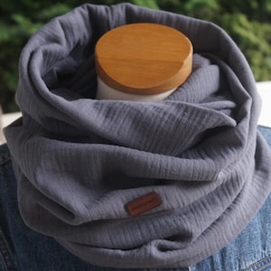 Könnte beinhalten: Grauer Baumwoll-Infinity-Schal mit einem braunen Lederanhänger mit der Aufschrift "Handcrafted".
