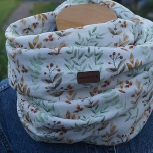Könnte beinhalten: Weißer Infinity-Schal mit einem braunen, grünen und weißen Blumenmuster. Der Schal hat ein braunes Leder-Etikett mit dem Text "mommoves" darauf.