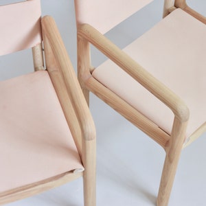 May include: Two wooden chairs with light pink fabric seats. The chairs have a simple, modern design with rounded edges.