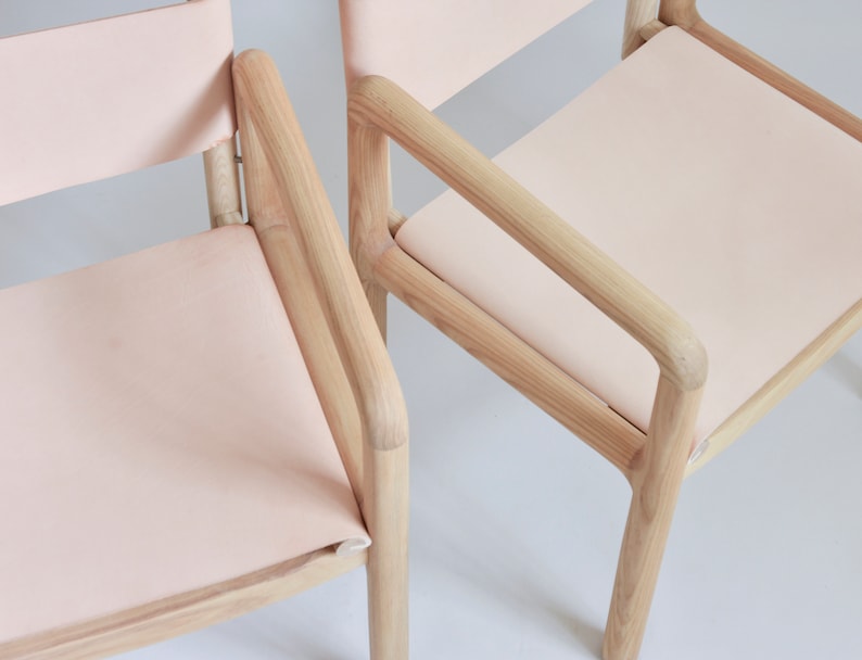 May include: Two wooden chairs with light pink fabric seats. The chairs have a simple, modern design with rounded edges.