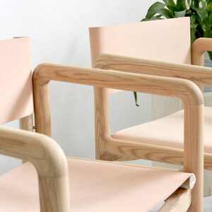 May include: Three wooden chairs with light pink leather seats and backs. The chairs have a simple, modern design with rounded edges.