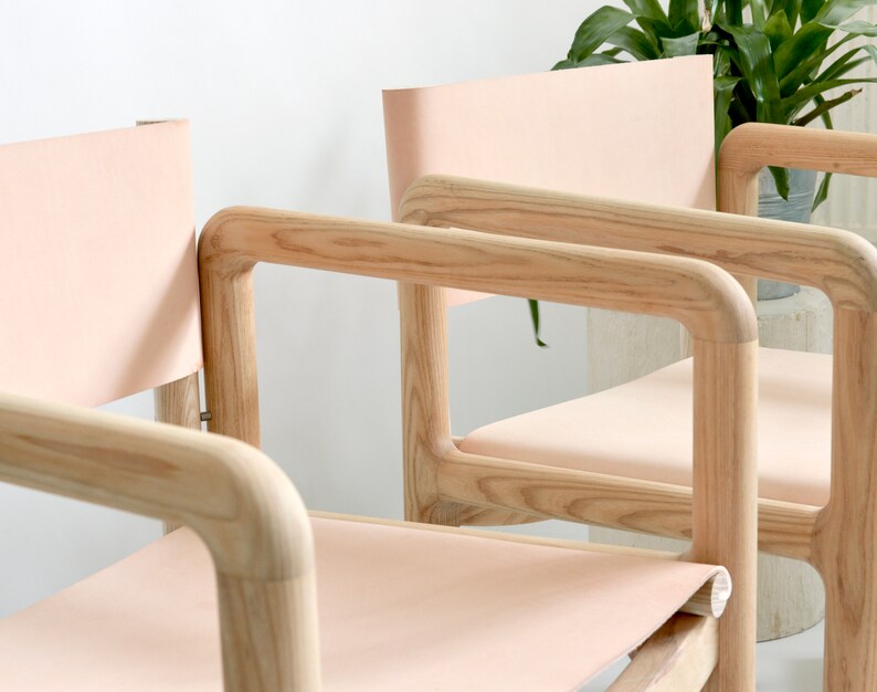 May include: Three wooden chairs with light pink leather seats and backs. The chairs have a simple, modern design with rounded edges.