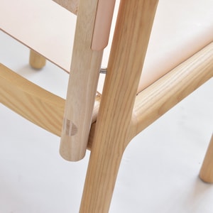 May include: Close-up of a wooden chair with a light brown finish. The chair has a curved back and a simple design. The chair is made of solid wood and has a natural grain pattern.