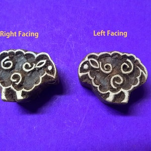 May include: Two wooden block printing stamps, one facing right and one facing left, both depicting a sheep with a curly design. The stamps are brown with white details.