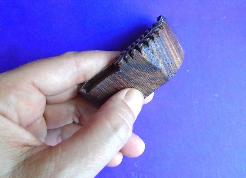 May include: A dark brown wooden comb with a textured surface. The comb has a series of teeth on one side and is held in a hand.