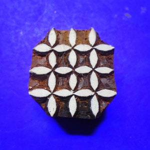 May include: A wooden block printing stamp with a geometric pattern of white flowers on a brown background.