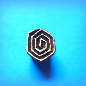 May include: A black wooden block with a carved design of a spiral pattern. The block is on a blue background.