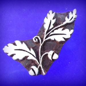 May include: A brown wooden block with a white design of a leafy branch with acorns. The block is used for printing patterns on fabric.
